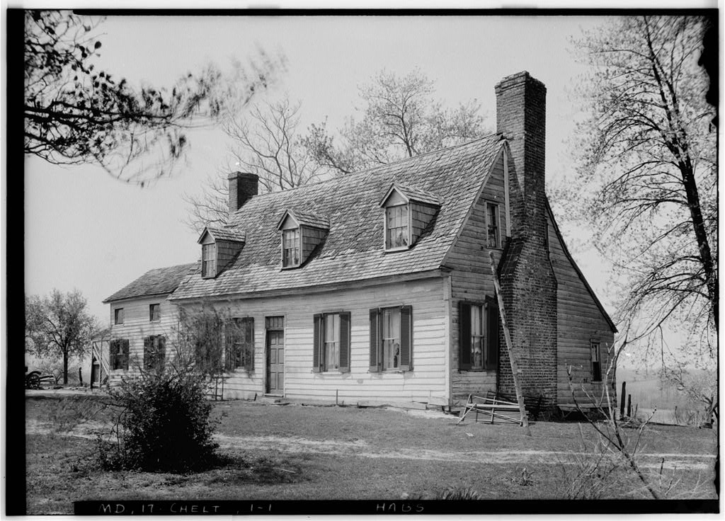 black and white photo of house with prominant chimney several windows with shutters on lower lever and in dormers on second floor